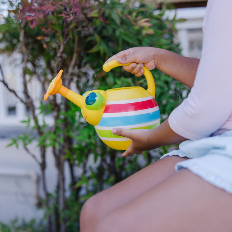 A kid playing with the Melissa & Doug Sunny Patch Giddy Buggy Watering Can With Flower-Shaped Spout