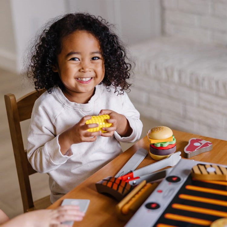 A kid playing with the Melissa & Doug Grill and Serve BBQ Set (20 pcs) - Wooden Play Food and Accessories