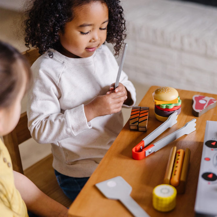 A kid playing with the Melissa & Doug Grill and Serve BBQ Set (20 pcs) - Wooden Play Food and Accessories