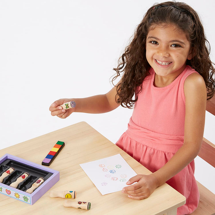 A child on white background with the Melissa & Doug Happy Handles Wooden Stamp Set: 6 Stamps and 6-Color Stamp Pad