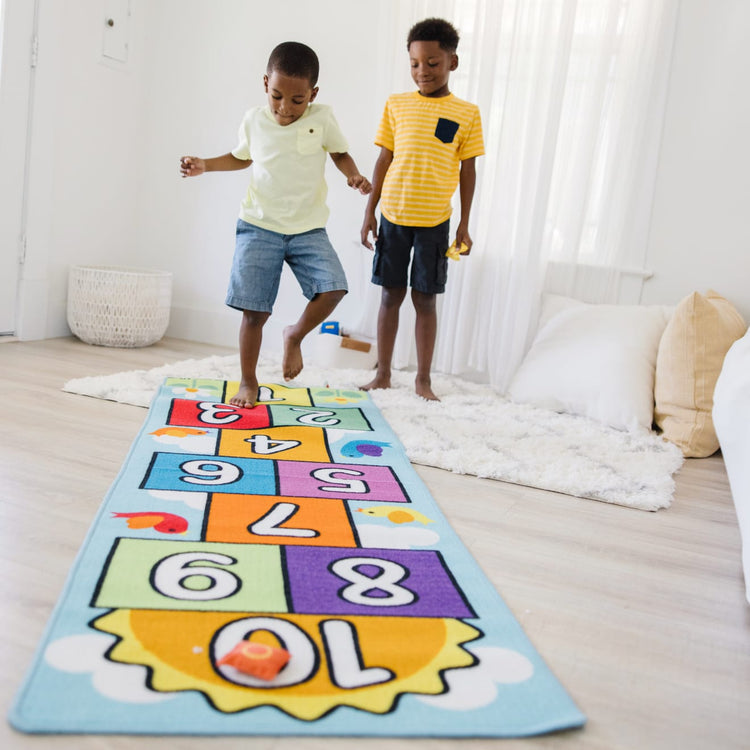 A kid playing with the Melissa & Doug Hop and Count Hopscotch Game Rug  (3 pcs, 78.5 x 26.5 inches)