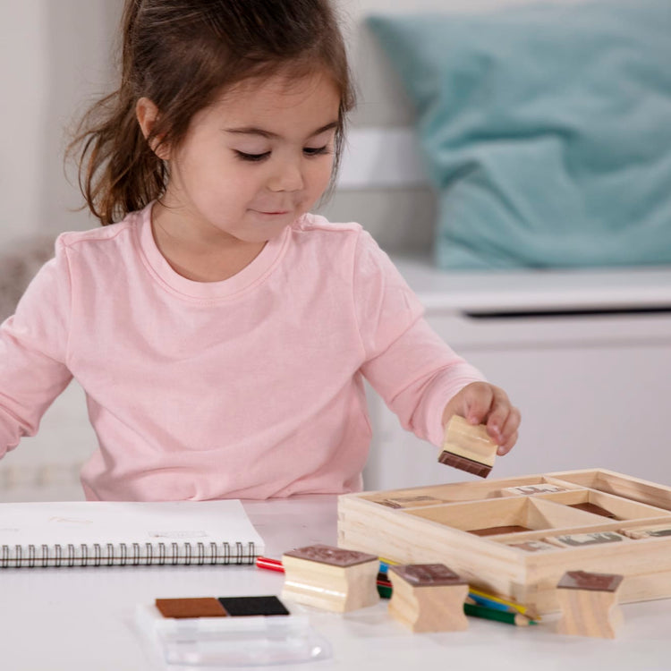 A kid playing with the Melissa & Doug Wooden Stamp Activity Set: Horses - 10 Stamps, 5 Colored Pencils, 2-Color Stamp Pad