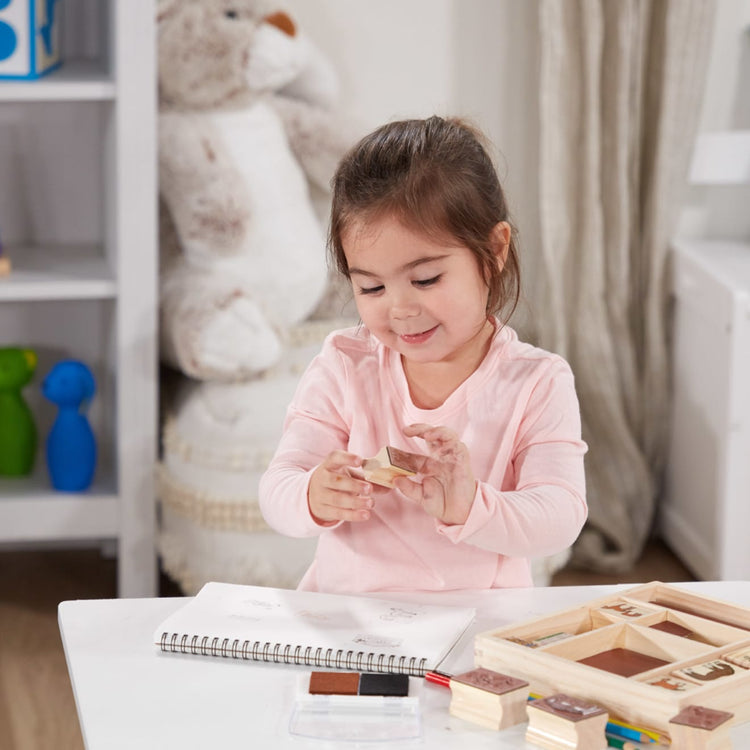 A kid playing with the Melissa & Doug Wooden Stamp Activity Set: Horses - 10 Stamps, 5 Colored Pencils, 2-Color Stamp Pad