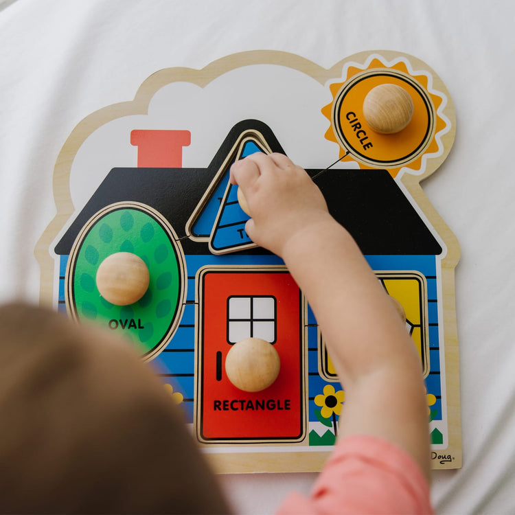 A kid playing with the Melissa & Doug Jumbo Knob Wooden Puzzles Set - Shapes and Barn