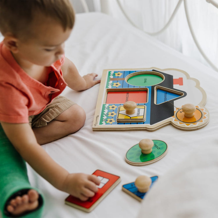 A kid playing with the Melissa & Doug Jumbo Knob Wooden Puzzles Set - Shapes and Barn