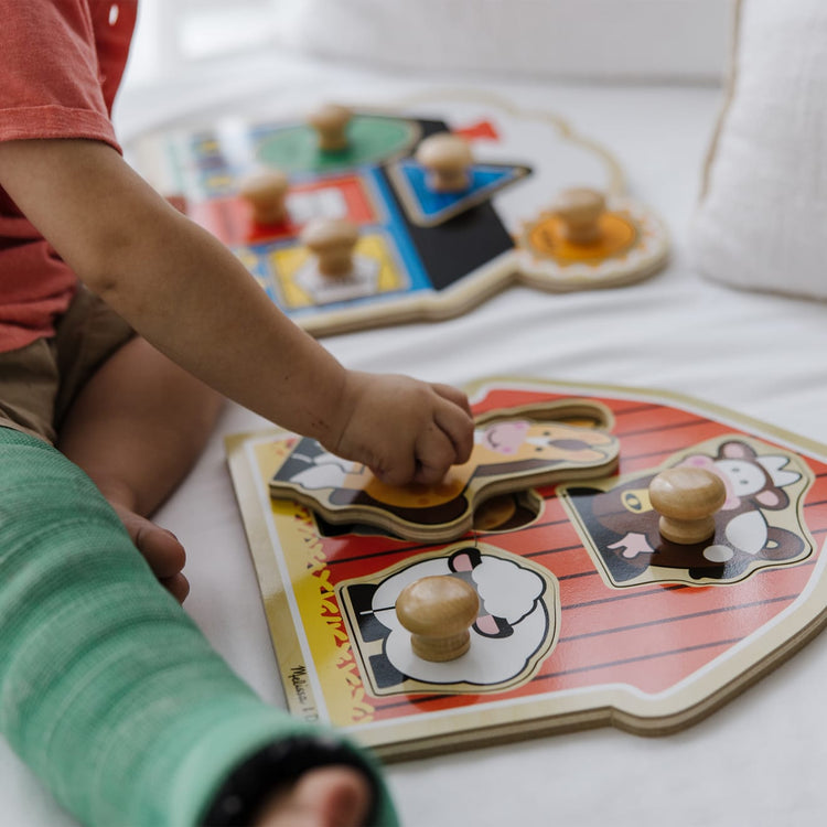 A kid playing with the Melissa & Doug Jumbo Knob Wooden Puzzles Set - Shapes and Barn