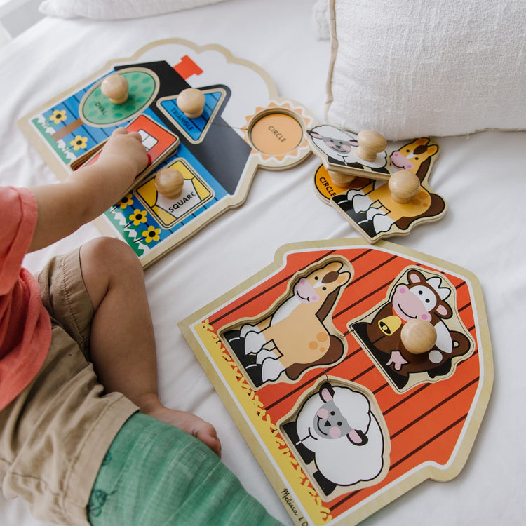 A kid playing with the Melissa & Doug Jumbo Knob Wooden Puzzles Set - Shapes and Barn