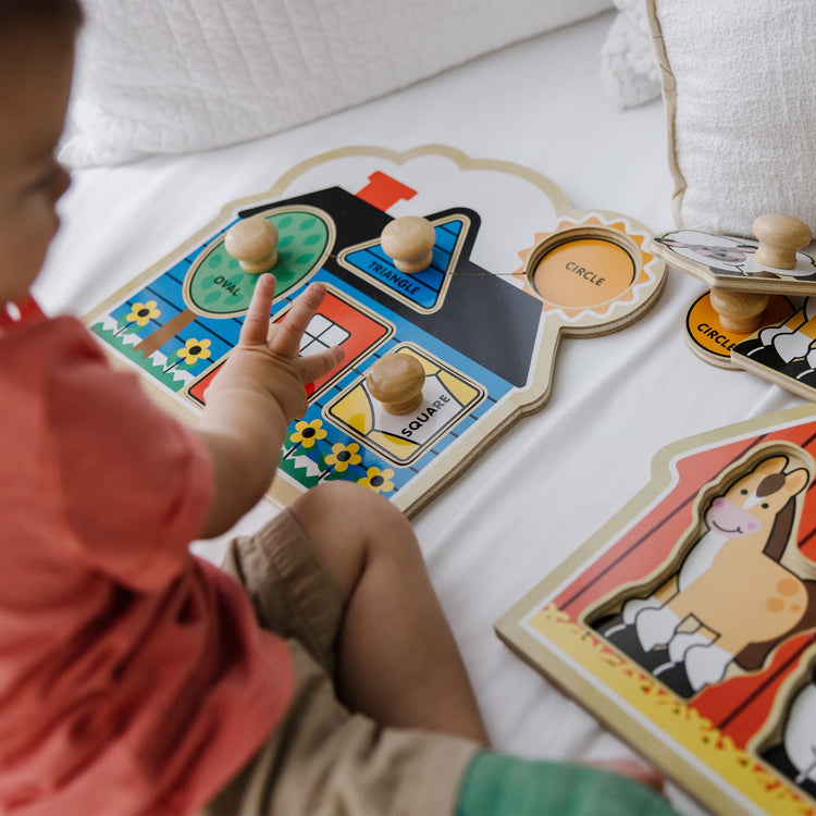 A kid playing with the Melissa & Doug Jumbo Knob Wooden Puzzles Set - Shapes and Barn