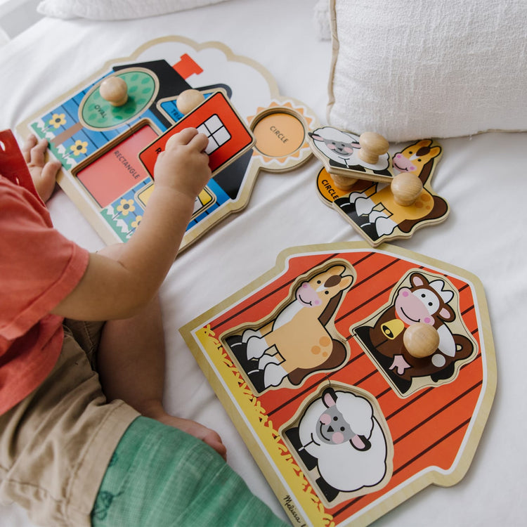 A kid playing with the Melissa & Doug Jumbo Knob Wooden Puzzles Set - Shapes and Barn