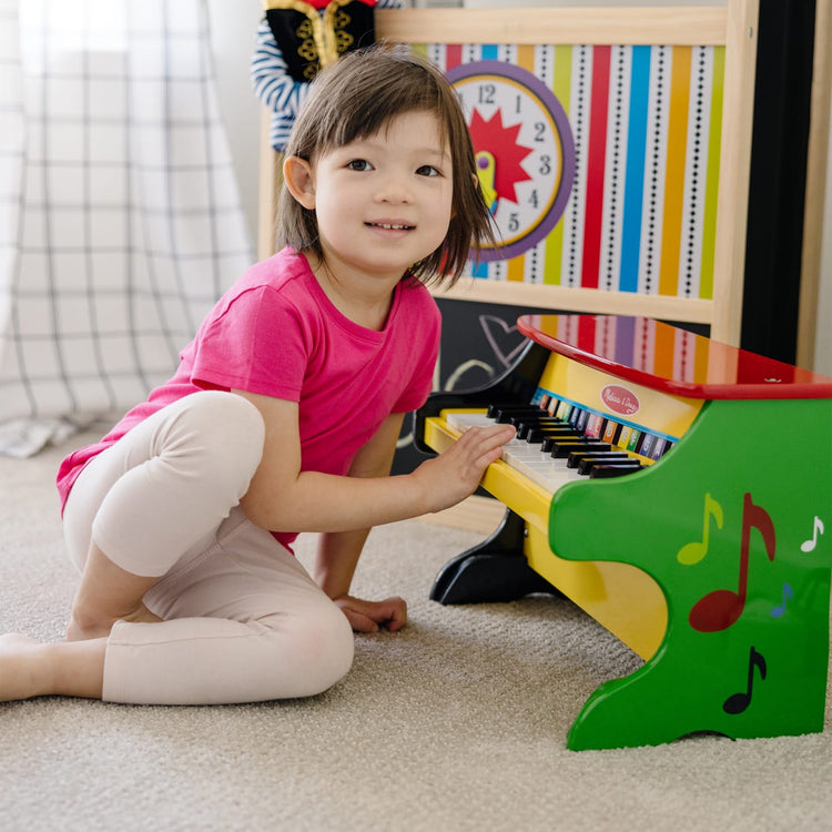 A kid playing with the Melissa & Doug Learn-To-Play Toy Piano With 25 Keys and Color-Coded Songbook