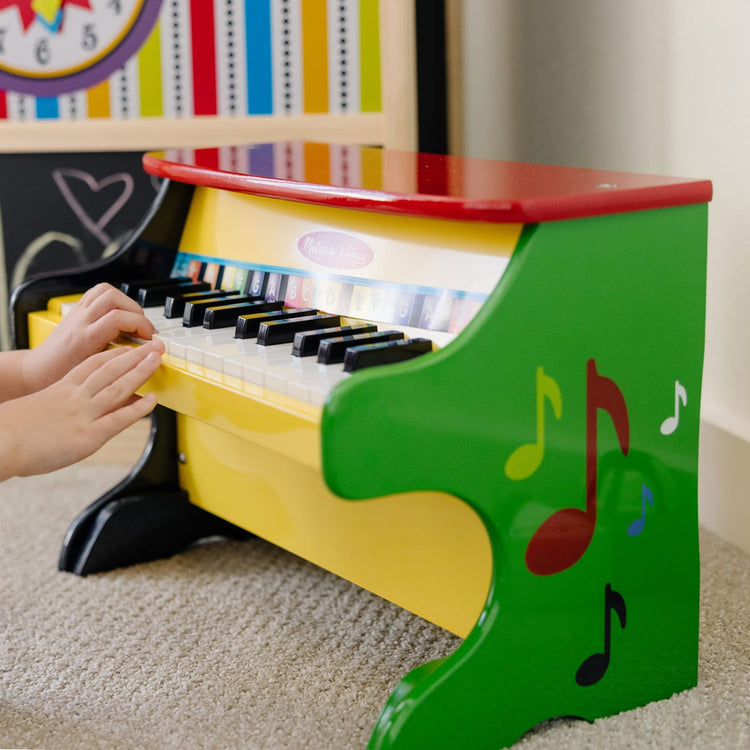 A kid playing with the Melissa & Doug Learn-To-Play Toy Piano With 25 Keys and Color-Coded Songbook