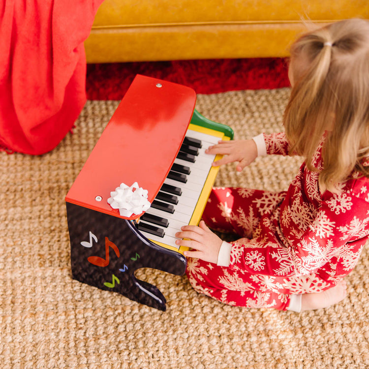 A kid playing with the Melissa & Doug Learn-To-Play Toy Piano With 25 Keys and Color-Coded Songbook