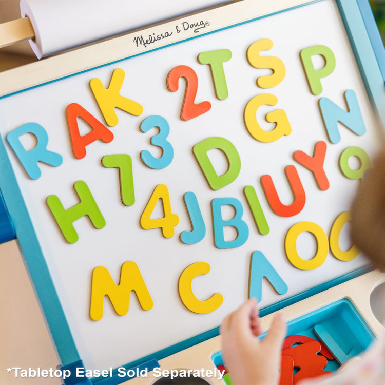 A kid playing with the Melissa & Doug Wooden Magnetic Letters and Numbers 2-Pack (89 Magnets)