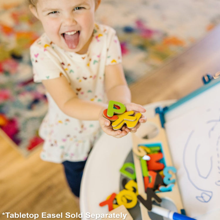 A kid playing with the Melissa & Doug Wooden Magnetic Letters and Numbers 2-Pack (89 Magnets)