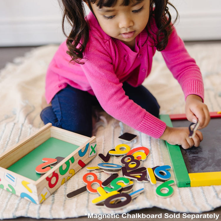 A kid playing with the Melissa & Doug Wooden Magnetic Letters and Numbers 2-Pack (89 Magnets)