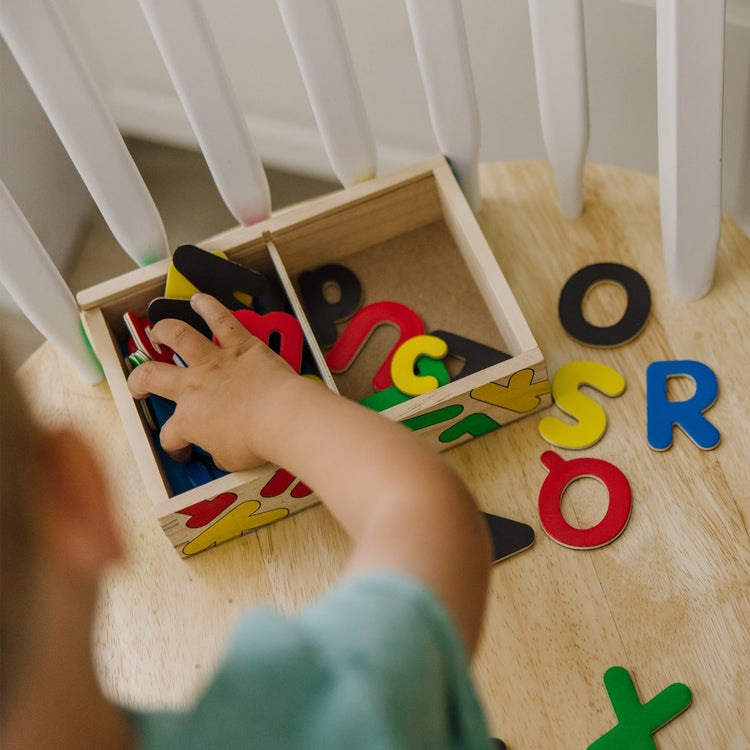 A kid playing with the Melissa & Doug Wooden Magnetic Letters and Numbers 2-Pack (89 Magnets)