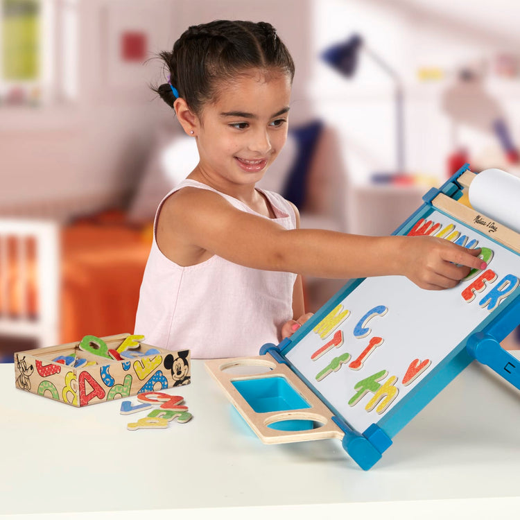 A kid playing with the Melissa & Doug Disney Mickey and Friends Wooden Alphabet Magnets - 52 Uppercase and Lowercase Letters