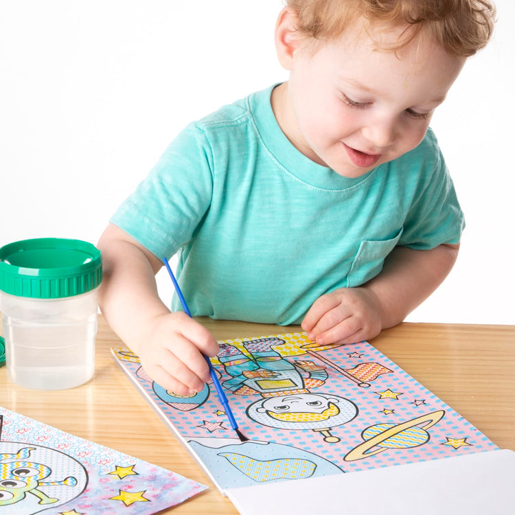 A child on white background with the Melissa & Doug My First Paint With Water Kids' Art Pad With Paintbrush - Pirates, Space, Construction, and More