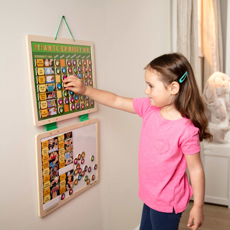 A kid playing with the Melissa & Doug Deluxe Wooden Magnetic Responsibility Chart With 90 Magnets