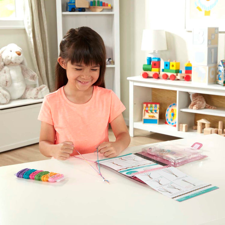 A kid playing with the Melissa & Doug On the Go Friendship Bracelet Craft Set (Makes 10+ Bracelets)