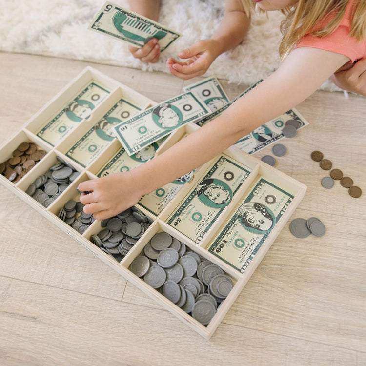 A kid playing with the Melissa & Doug Play Money Set - Educational Toy With Paper Bills and Plastic Coins (50 of Each Denomination) and Wooden Cash Drawer for Storage