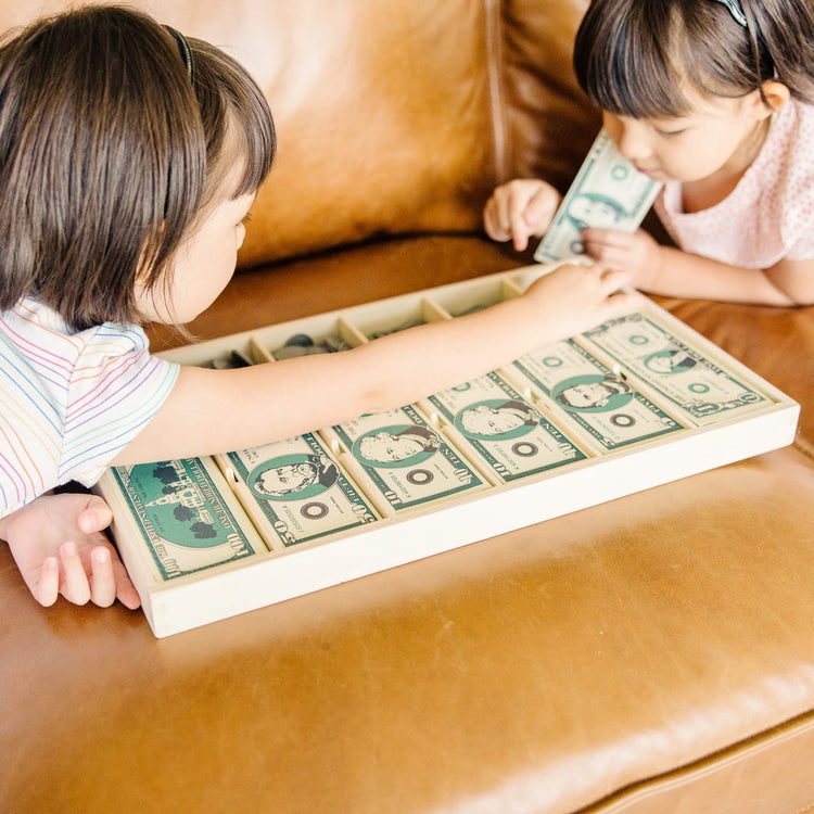 A kid playing with the Melissa & Doug Play Money Set - Educational Toy With Paper Bills and Plastic Coins (50 of Each Denomination) and Wooden Cash Drawer for Storage