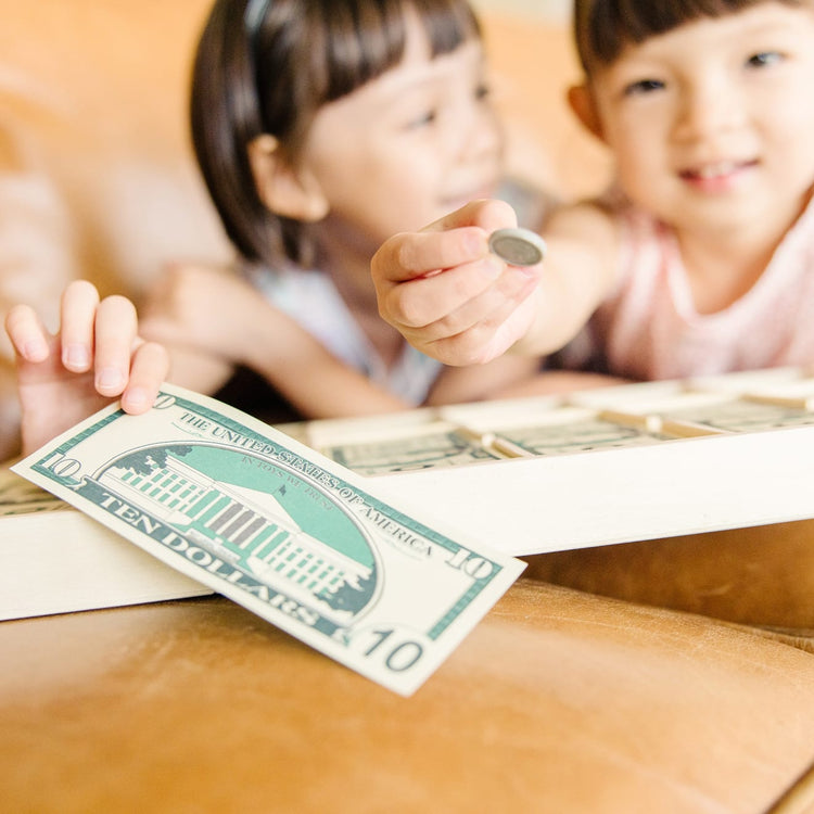 A kid playing with the Melissa & Doug Play Money Set - Educational Toy With Paper Bills and Plastic Coins (50 of Each Denomination) and Wooden Cash Drawer for Storage