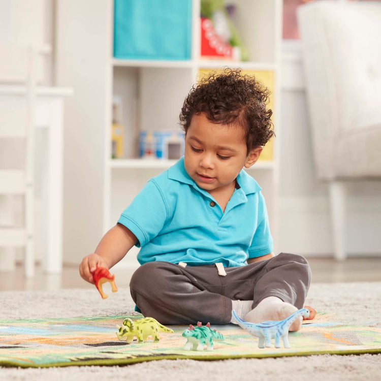 A kid playing with the Melissa & Doug Prehistoric Playground Dinosaur Activity Rug (39 x 36 inches) - 4 Toy Animals