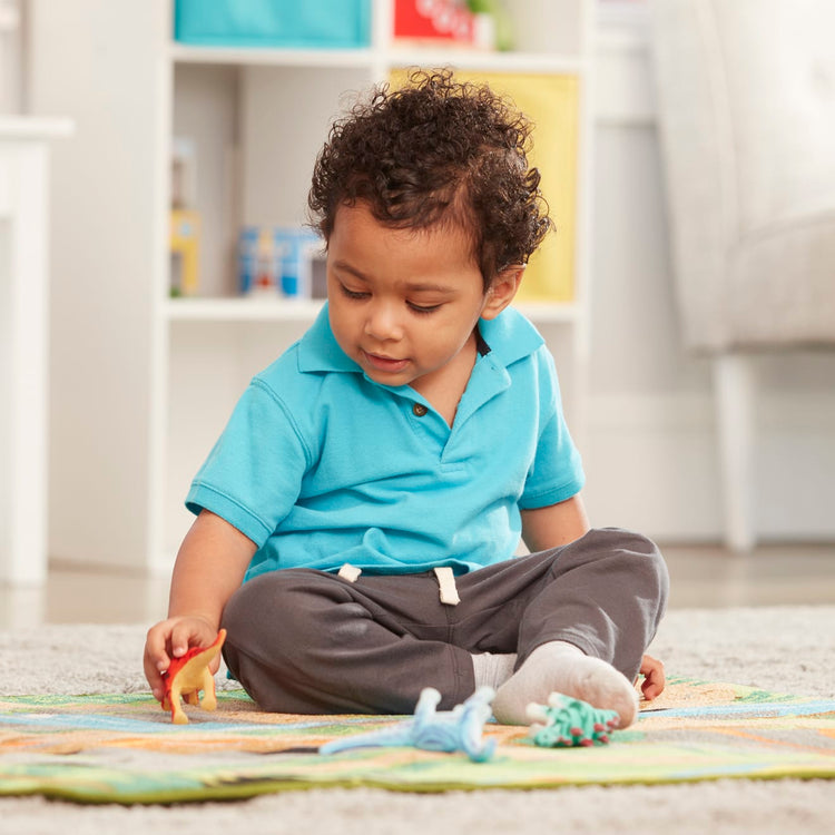 A kid playing with the Melissa & Doug Prehistoric Playground Dinosaur Activity Rug (39 x 36 inches) - 4 Toy Animals