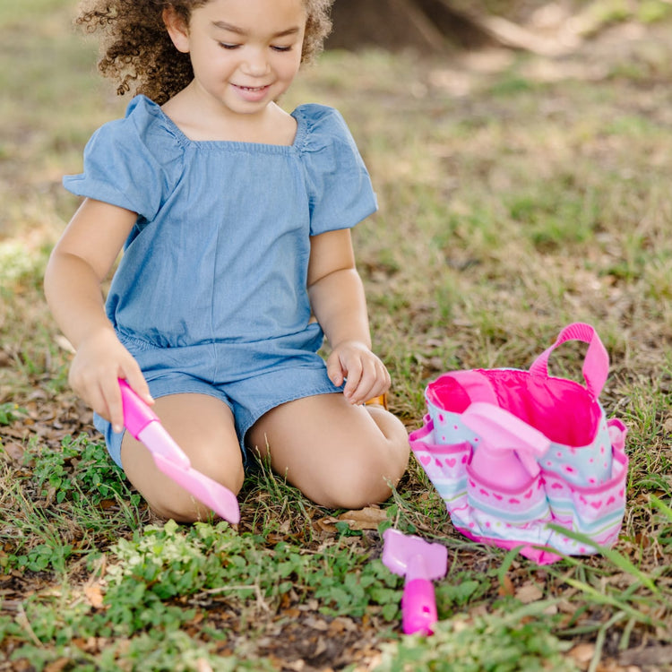 A kid playing with the Melissa & Doug Sunny Patch Pretty Petals Gardening Tote Set With Tools