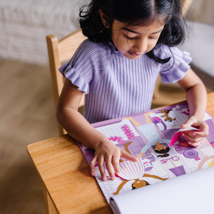 A kid playing with the Melissa & Doug Reusable Sticker Pad: Dress-Up - 165+ Reusable Stickers