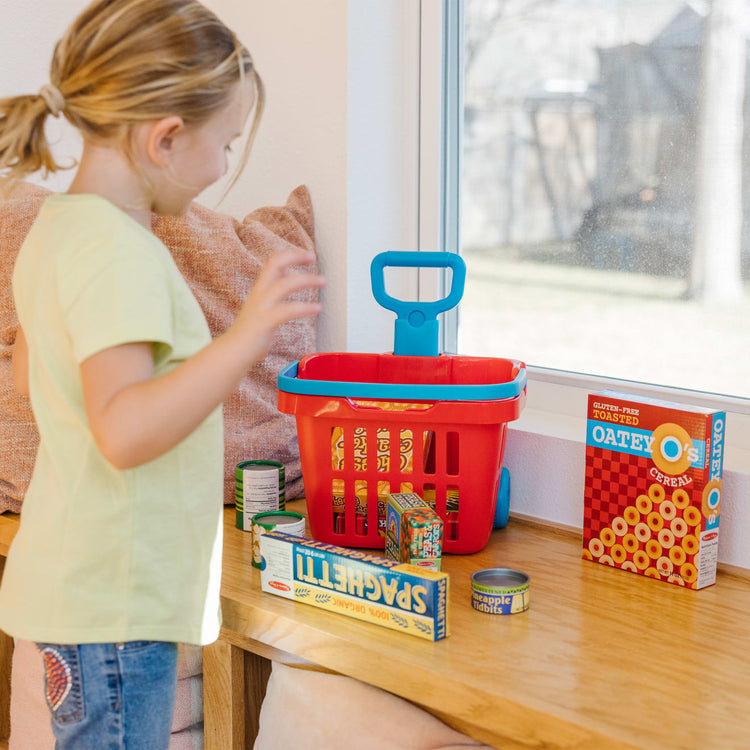 A kid playing with the Melissa & Doug Fill and Roll Grocery Basket Play Set With Play Food Boxes and Cans (11 pcs)