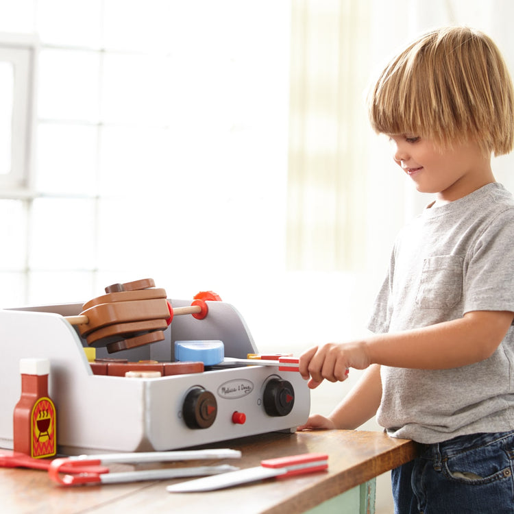 A kid playing with the Melissa & Doug Rotisserie and Grill Wooden Barbecue Play Food Set (24 pcs)