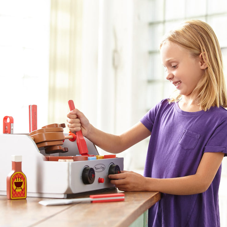 A kid playing with the Melissa & Doug Rotisserie and Grill Wooden Barbecue Play Food Set (24 pcs)