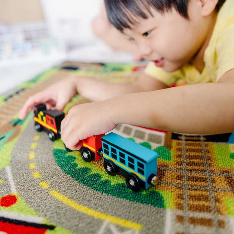 A kid playing with the Melissa & Doug Round the Rails Train Rug With 3 Linking Wooden Train Cars  (39 x 36 inches)