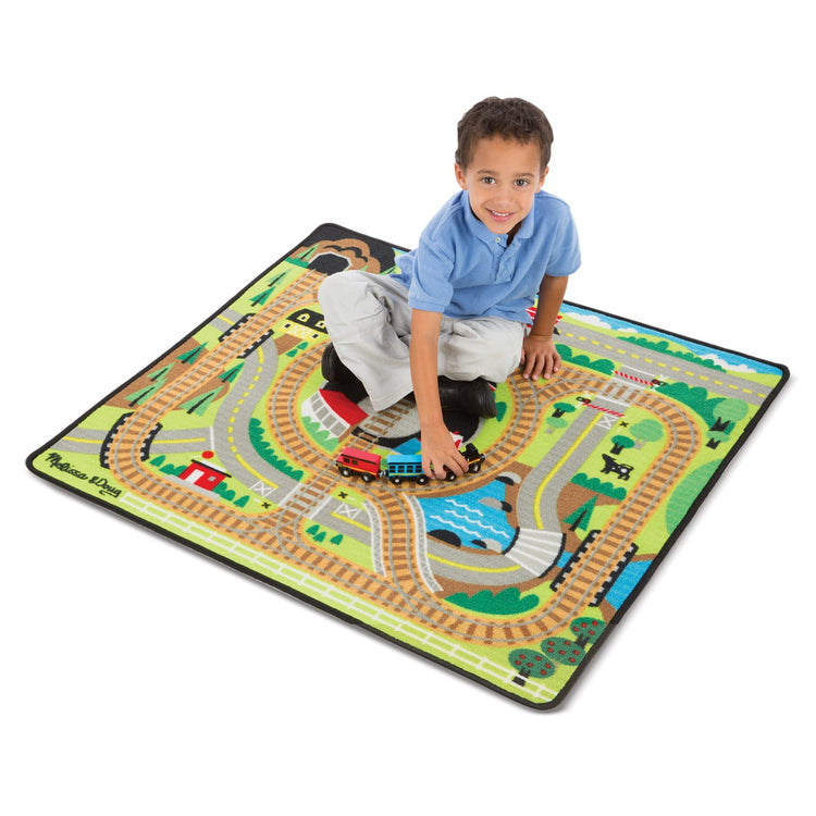 A child on white background with the Melissa & Doug Round the Rails Train Rug With 3 Linking Wooden Train Cars  (39 x 36 inches)