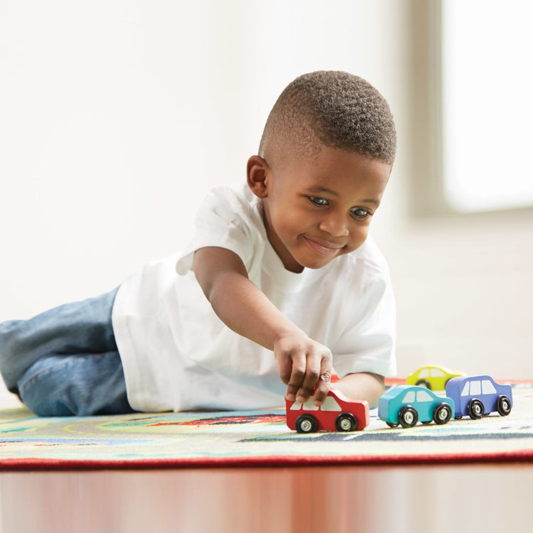 A kid playing with the Melissa & Doug Round the Town Road Rug and Car Activity Play Set With 4 Wooden Cars (39 x 36 inches)