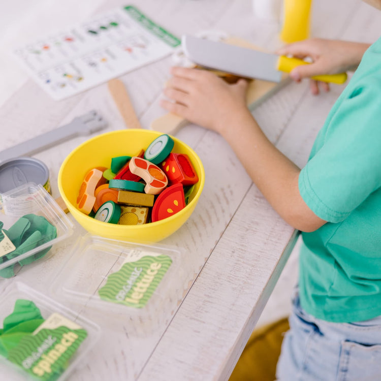 A kid playing with the Melissa & Doug Slice and Toss Salad Play Food Set – 52 Wooden and Felt Pieces