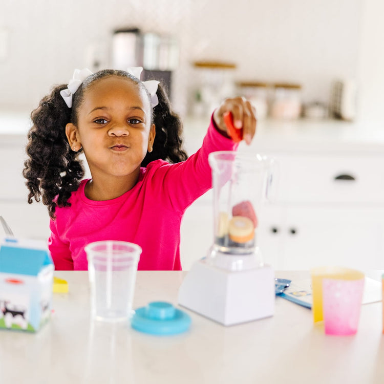 A kid playing with the Melissa & Doug Smoothie Maker Blender Set with Play Food (222 Pcs)