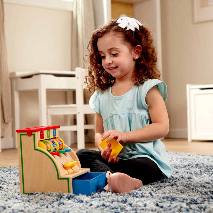 A kid playing with the Melissa & Doug Spin and Swipe Wooden Toy Cash Register With 3 Play Coins, Pretend Credit Card