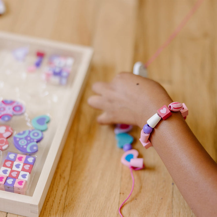 The front of the box for the Melissa & Doug Created by Me! Heart Beads Wooden Bead Kit, 120+ Beads and 5 Cords for Jewelry-Making