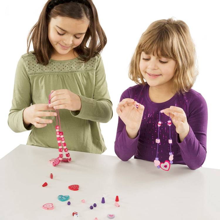 A child on white background with the Melissa & Doug Created by Me! Heart Beads Wooden Bead Kit, 120+ Beads and 5 Cords for Jewelry-Making