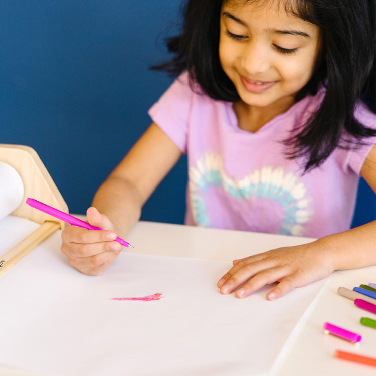 A kid playing with the Melissa & Doug Wooden Tabletop Paper Roll Dispenser With White Bond Paper (12 inches x 75 feet)