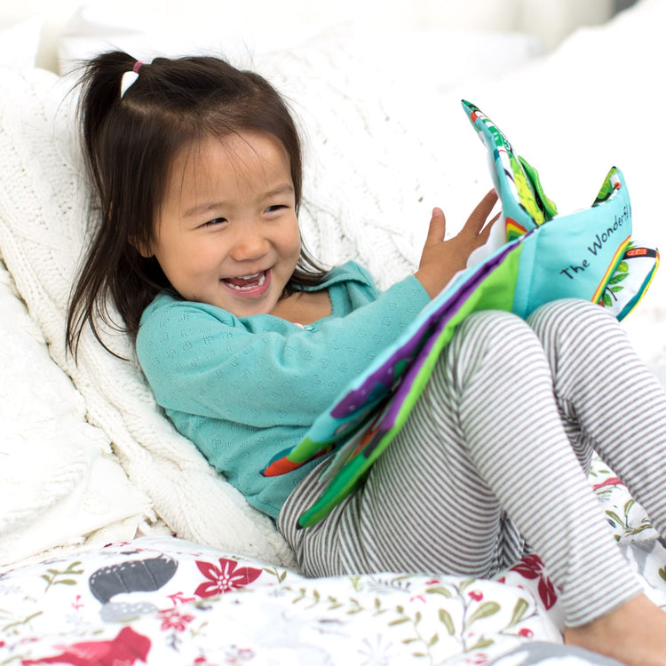 A kid playing with the Melissa & Doug Soft Activity Baby Book - The Wonderful World of Peekaboo!