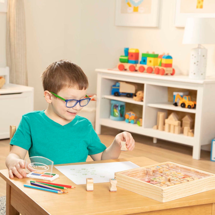 A kid playing with the Melissa & Doug Wooden Stamp Set, Favorite Things - 26 Wooden Stamps, 4-Color Stamp Pad