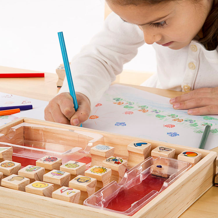 A child on white background with the Melissa & Doug Wooden Stamp Set, Favorite Things - 26 Wooden Stamps, 4-Color Stamp Pad