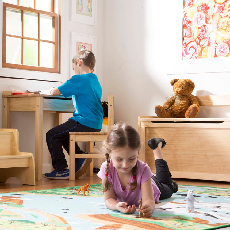 A kid playing with the Melissa & Doug Wooden Child's Lift-Top Desk & Chair - Honey