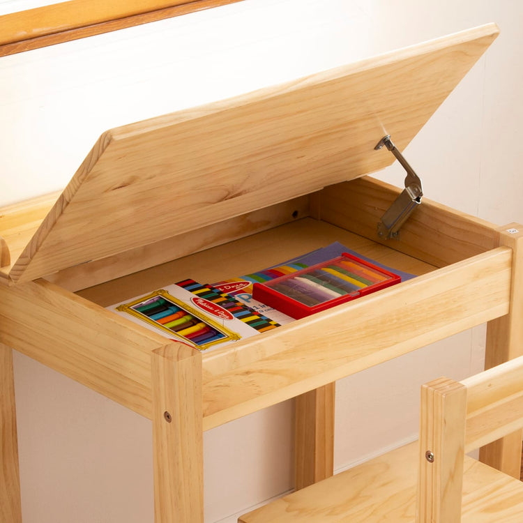 A kid playing with the Melissa & Doug Wooden Child's Lift-Top Desk & Chair - Honey