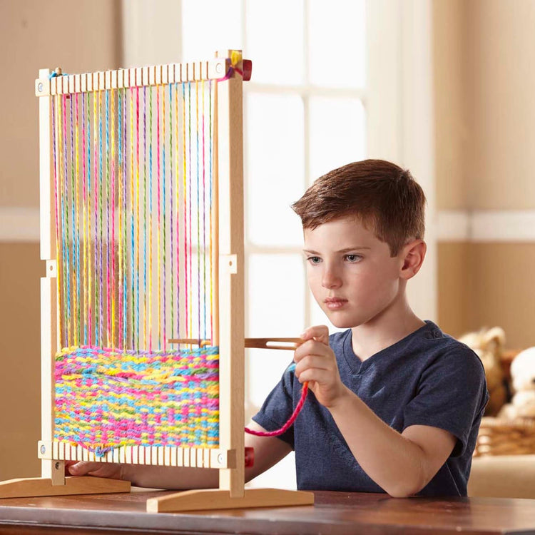 A kid playing with the Melissa & Doug Wooden Multi-Craft Weaving Loom: Extra-Large Frame (22.75 x 16.5 inches)