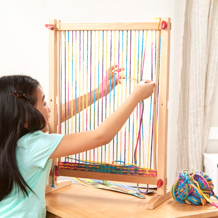 A kid playing with the Melissa & Doug Wooden Multi-Craft Weaving Loom: Extra-Large Frame (22.75 x 16.5 inches)